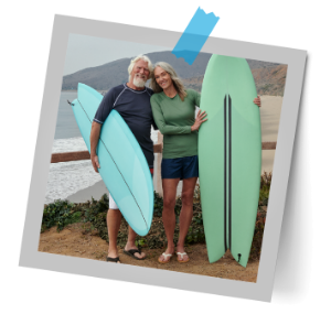 An elderly couple standing at beach with surfing boards