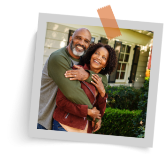 A man with a warm smile embraces a woman from behind, both with joyful expressions